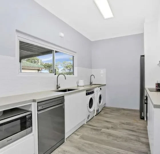 Modern laundry room renovation with white cabinets, built-in washing machines, sink, and minimalist design