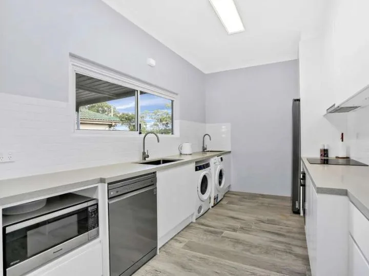 Modern laundry room renovation with white cabinets, built-in washing machines, sink, and minimalist design